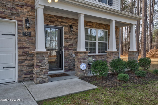 property entrance with covered porch, stone siding, and a garage