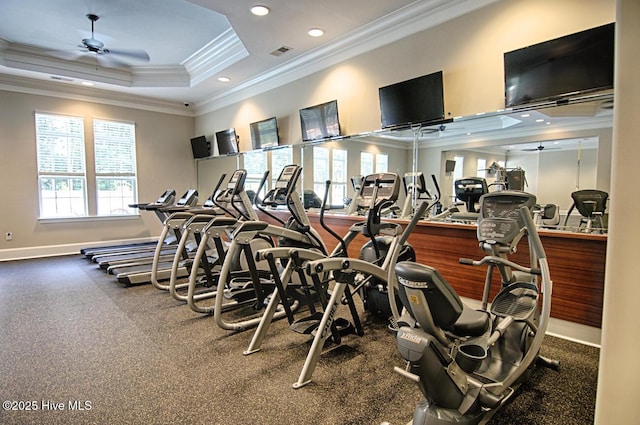 workout area with a raised ceiling, visible vents, ornamental molding, a ceiling fan, and baseboards