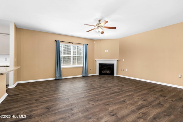 unfurnished living room with a fireplace, dark wood finished floors, a ceiling fan, and baseboards