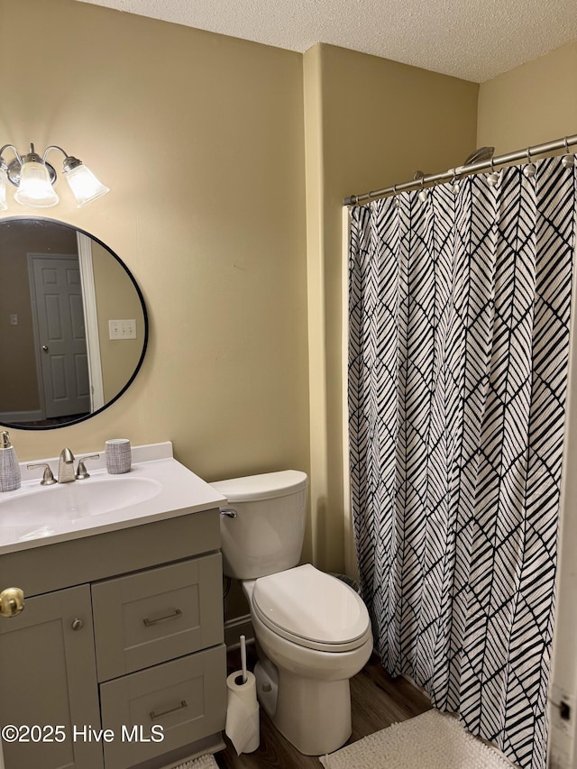 bathroom with wood-type flooring, vanity, walk in shower, toilet, and a textured ceiling