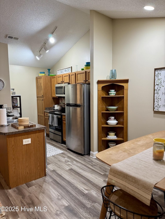 kitchen with vaulted ceiling, appliances with stainless steel finishes, track lighting, a textured ceiling, and light hardwood / wood-style flooring