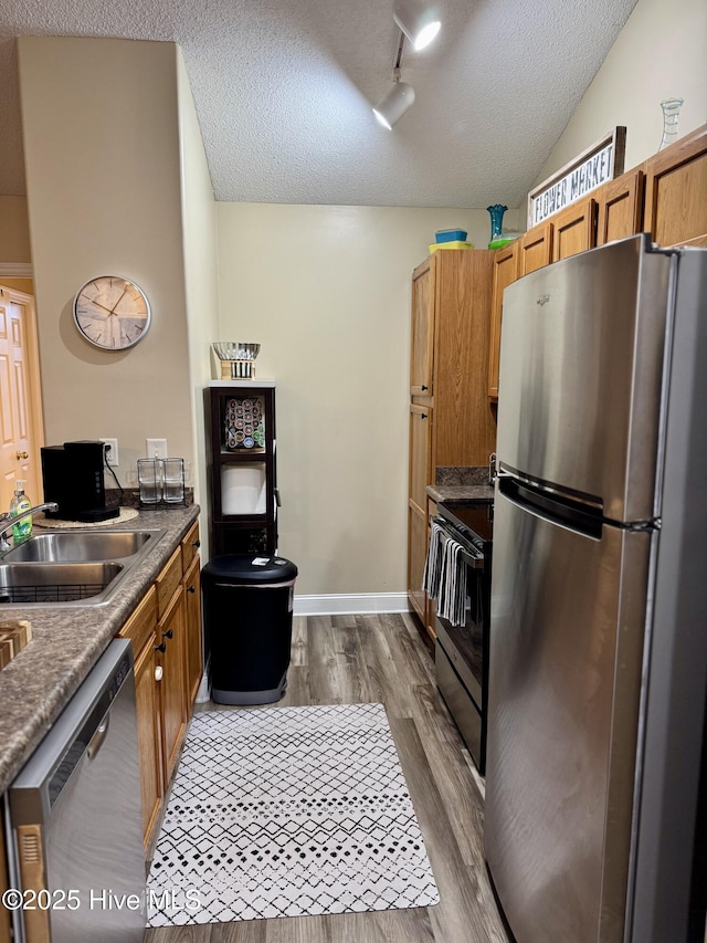 kitchen featuring lofted ceiling, sink, appliances with stainless steel finishes, wood-type flooring, and a textured ceiling