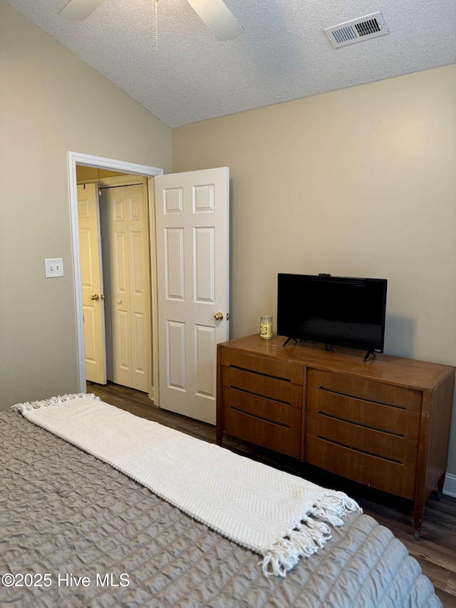 bedroom with lofted ceiling, ceiling fan, a textured ceiling, dark hardwood / wood-style flooring, and a closet