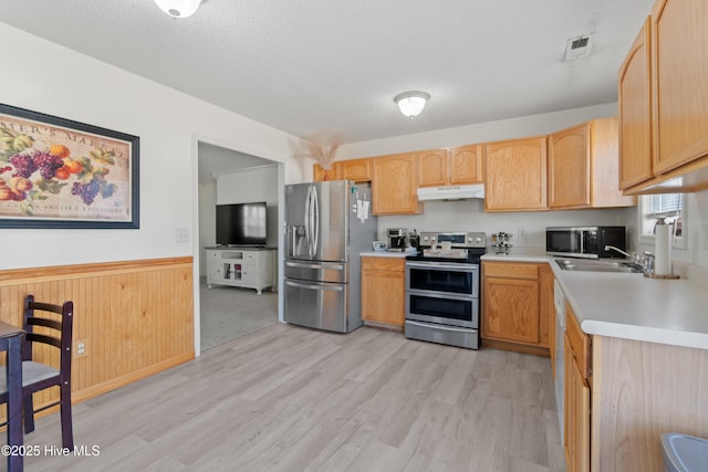 kitchen with light brown cabinetry, sink, stainless steel appliances, a textured ceiling, and light hardwood / wood-style flooring