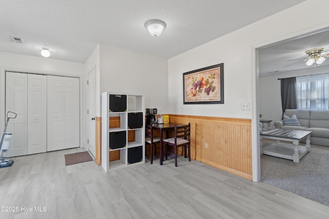 home office featuring ceiling fan, light hardwood / wood-style flooring, wooden walls, and a textured ceiling