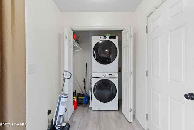 laundry area with stacked washer and clothes dryer, a textured ceiling, and light hardwood / wood-style flooring