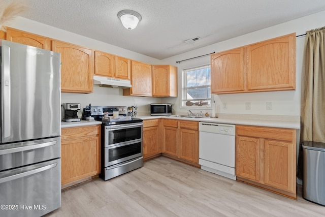 kitchen with light brown cabinetry, light hardwood / wood-style floors, a textured ceiling, and appliances with stainless steel finishes