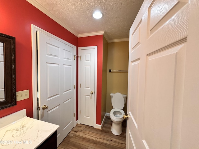 bathroom with hardwood / wood-style floors, vanity, ornamental molding, a textured ceiling, and toilet