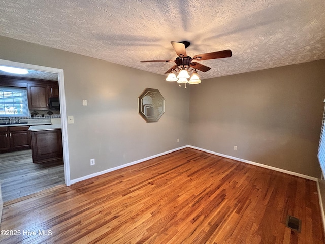 empty room with ceiling fan, sink, a textured ceiling, and light wood-type flooring