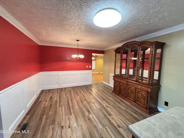 unfurnished dining area with hardwood / wood-style flooring, crown molding, a notable chandelier, and a textured ceiling