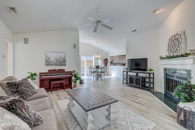 living room with high vaulted ceiling, a high end fireplace, ceiling fan with notable chandelier, and light wood-type flooring