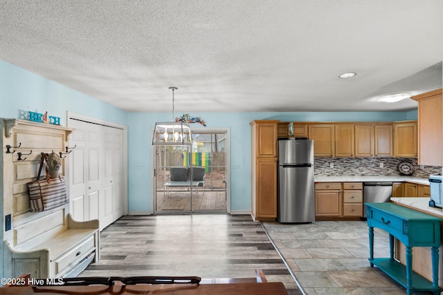 kitchen featuring decorative backsplash, hanging light fixtures, light hardwood / wood-style floors, stainless steel appliances, and a textured ceiling