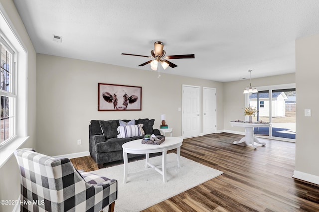 living room featuring ceiling fan with notable chandelier, dark wood-type flooring, and a textured ceiling