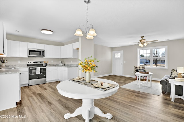 kitchen featuring sink, light hardwood / wood-style flooring, hanging light fixtures, stainless steel appliances, and white cabinets