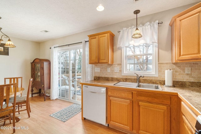 kitchen featuring pendant lighting, tasteful backsplash, sink, white dishwasher, and light hardwood / wood-style flooring