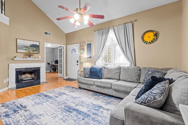 living room featuring a tile fireplace, high vaulted ceiling, wood-type flooring, and ceiling fan