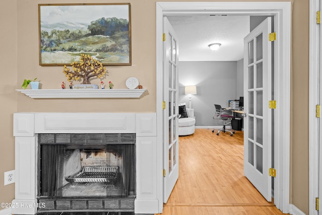 hallway with french doors, light hardwood / wood-style flooring, and a textured ceiling