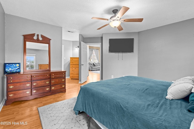 bedroom featuring ceiling fan, ensuite bath, light hardwood / wood-style floors, and a textured ceiling