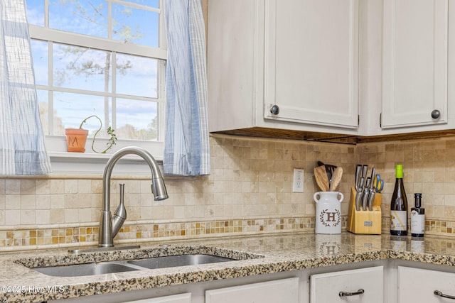 kitchen featuring tasteful backsplash, white cabinetry, light stone countertops, and sink