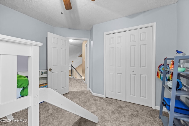 bedroom featuring ceiling fan, a closet, light carpet, and a textured ceiling