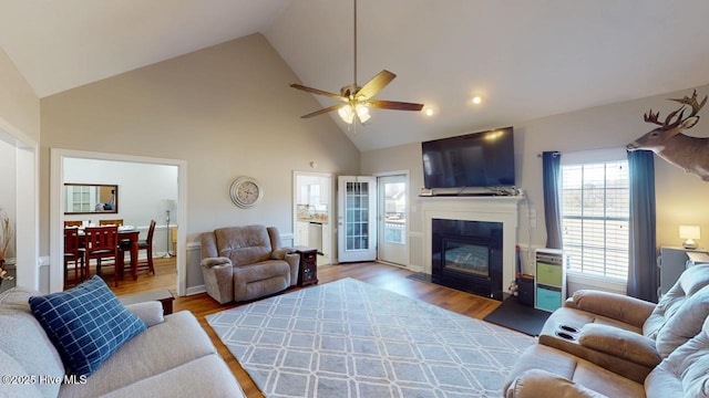 living room with ceiling fan, a large fireplace, high vaulted ceiling, and light hardwood / wood-style flooring