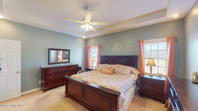 carpeted bedroom with ceiling fan and a tray ceiling