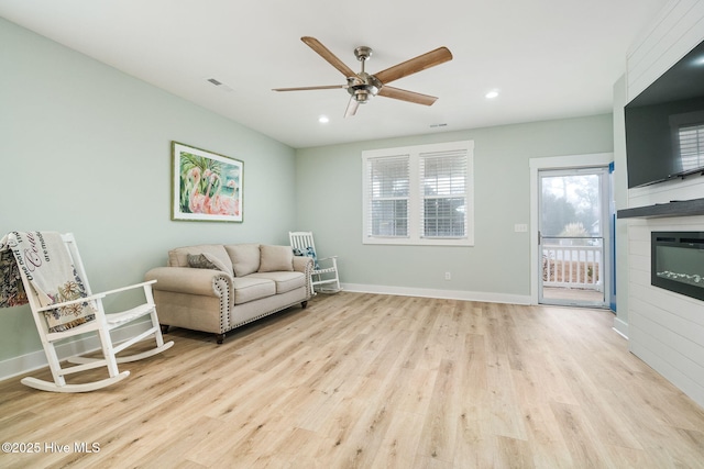 living room with light hardwood / wood-style floors, a large fireplace, and ceiling fan