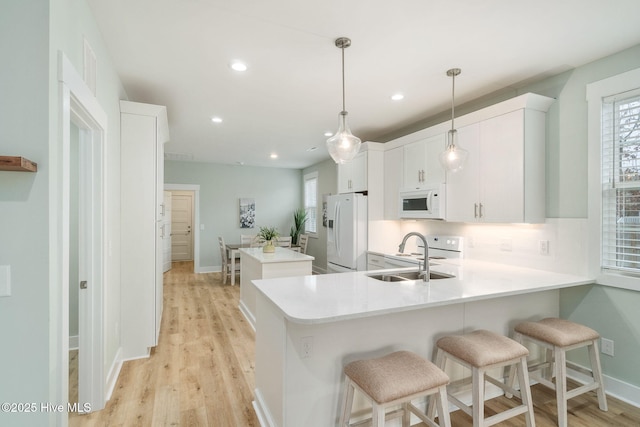 kitchen with white cabinetry, sink, hanging light fixtures, kitchen peninsula, and white appliances