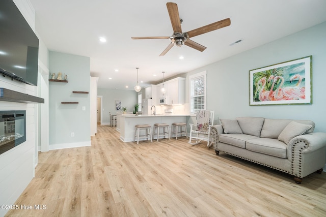 living room with a fireplace, ceiling fan, and light wood-type flooring