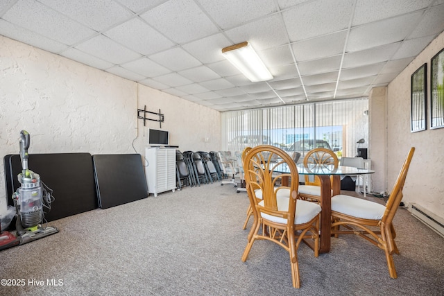 carpeted dining area with a drop ceiling and a baseboard heating unit