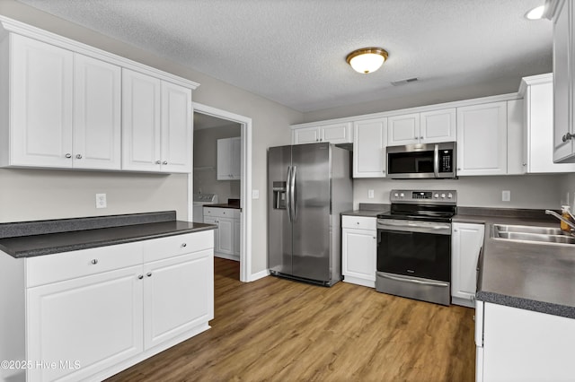 kitchen featuring stainless steel appliances, white cabinetry, wood-type flooring, and sink