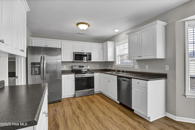 kitchen with appliances with stainless steel finishes, sink, white cabinets, and light hardwood / wood-style flooring