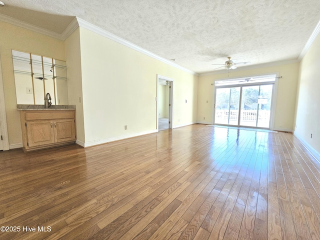 unfurnished living room with hardwood / wood-style floors, sink, ceiling fan, crown molding, and a textured ceiling