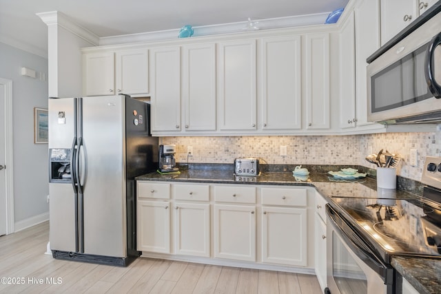 kitchen with stainless steel appliances, dark stone countertops, white cabinets, and backsplash