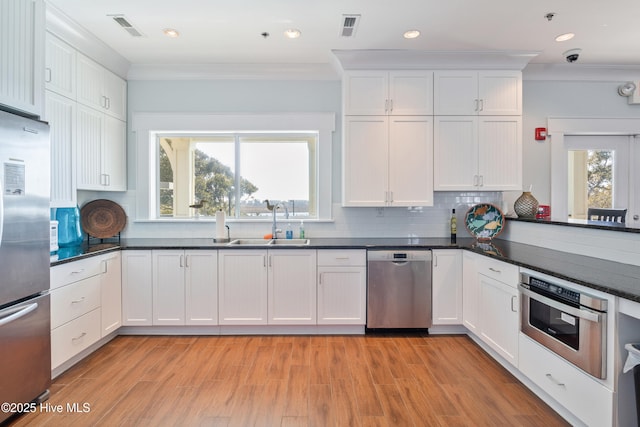 kitchen featuring stainless steel appliances, white cabinetry, backsplash, and crown molding