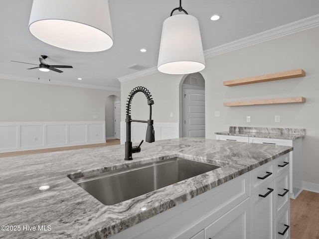 kitchen with crown molding, arched walkways, white cabinetry, light stone counters, and a sink
