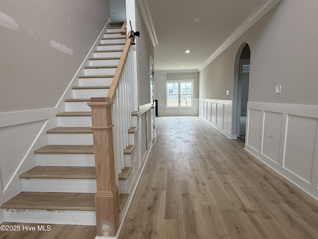 stairs featuring ornamental molding, wood finished floors, arched walkways, wainscoting, and a decorative wall