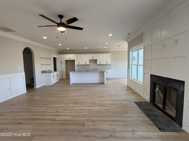 interior space with arched walkways, light wood-style flooring, a decorative wall, white cabinetry, and crown molding