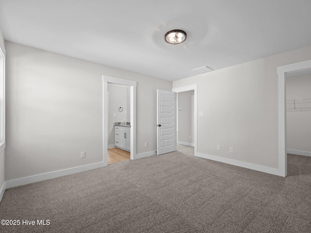 unfurnished bedroom featuring a closet, light colored carpet, ensuite bath, a spacious closet, and baseboards