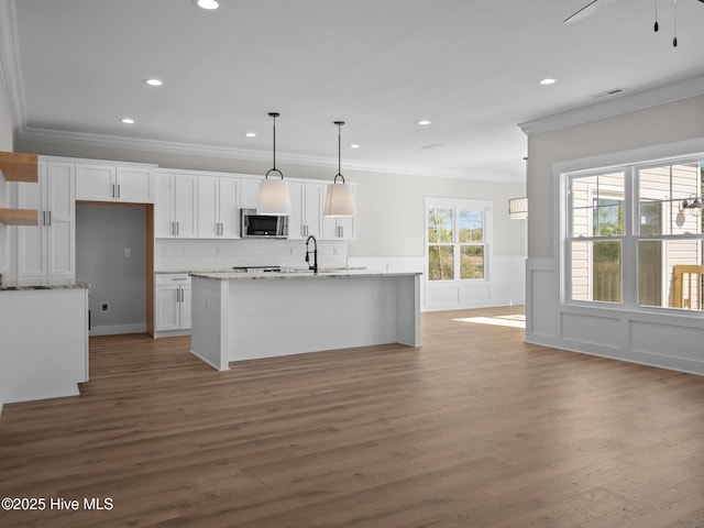 kitchen featuring crown molding, stainless steel microwave, white cabinets, and a center island with sink
