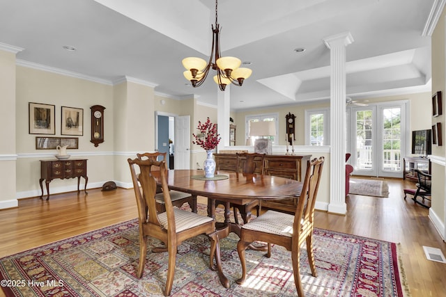 dining space with ornate columns, crown molding, a chandelier, a raised ceiling, and light hardwood / wood-style floors