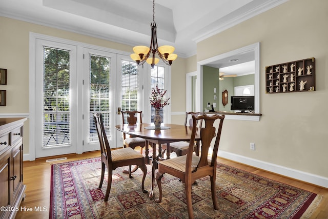 dining area with an inviting chandelier, a tray ceiling, light hardwood / wood-style flooring, and ornamental molding