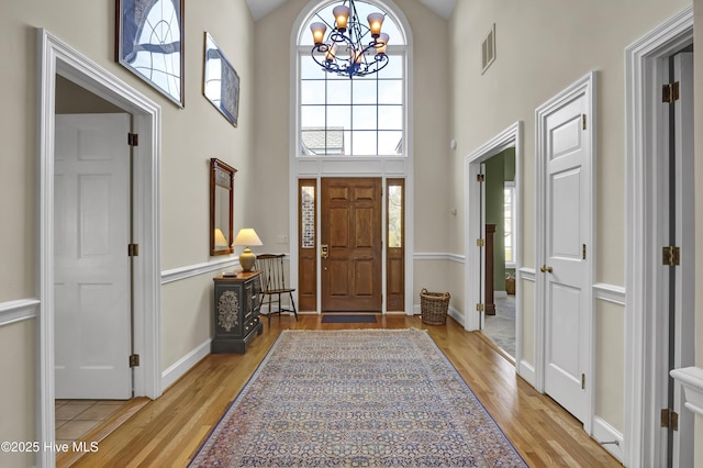 foyer entrance with a notable chandelier, a towering ceiling, and light wood-type flooring