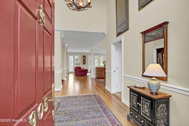 entrance foyer featuring decorative columns, a towering ceiling, a notable chandelier, and light hardwood / wood-style flooring