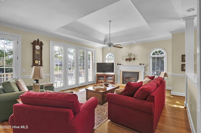 living room featuring crown molding, hardwood / wood-style flooring, ceiling fan, decorative columns, and a raised ceiling