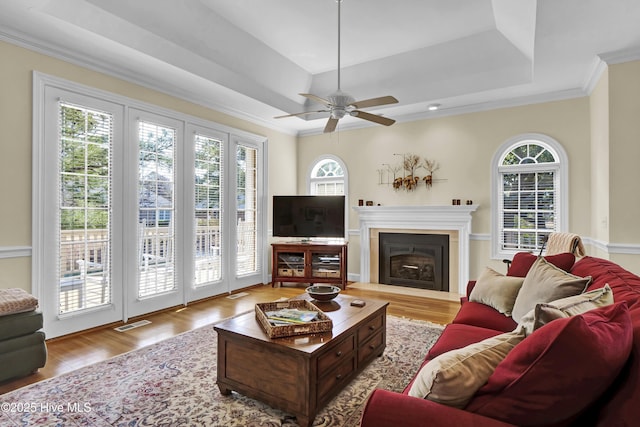 living room with a tray ceiling, ornamental molding, ceiling fan, and light wood-type flooring