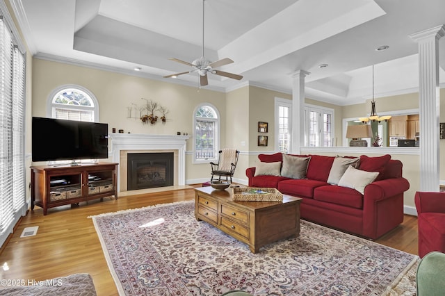 living room featuring crown molding, a raised ceiling, light hardwood / wood-style floors, and ornate columns