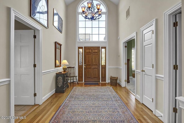 entryway with a towering ceiling, a notable chandelier, and light hardwood / wood-style flooring