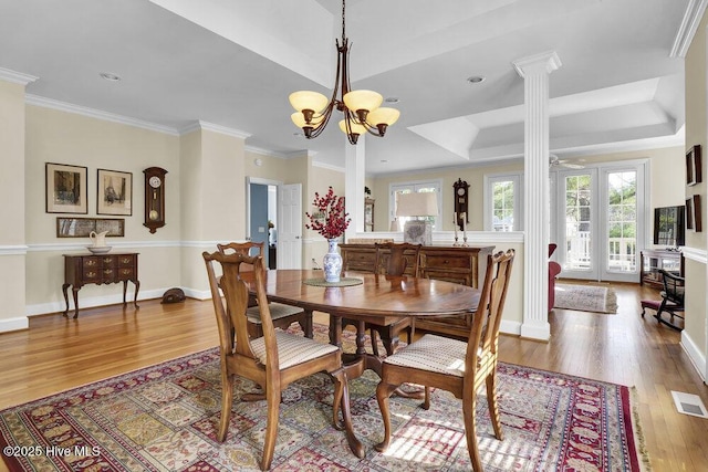 dining space featuring decorative columns, a notable chandelier, light hardwood / wood-style floors, a tray ceiling, and crown molding