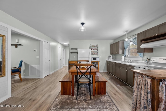 kitchen featuring hanging light fixtures, exhaust hood, white appliances, and light hardwood / wood-style floors